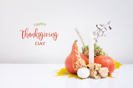 Autumn composition with Happy Thanksgiving Day greeting text. Dried leaves, pumpkins and candles on white backgroundの写真素材