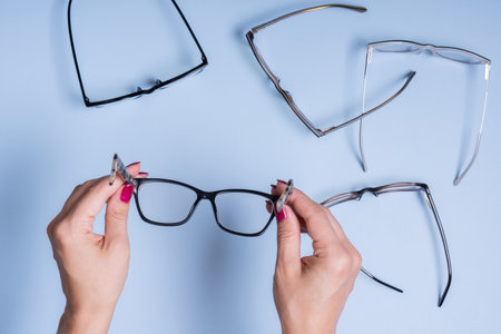 Eyeglasses in female hand on blue background. Optical store, vision test, stylish glasses concept.