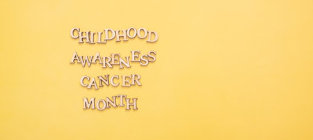 Childhood cancer awareness month text from wooden letters on yellow background with copy space