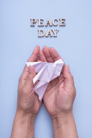 Peace day text from wooden letters with white paper dove in female hands on blue background. International Peace day concept. Vertical formatの写真素材