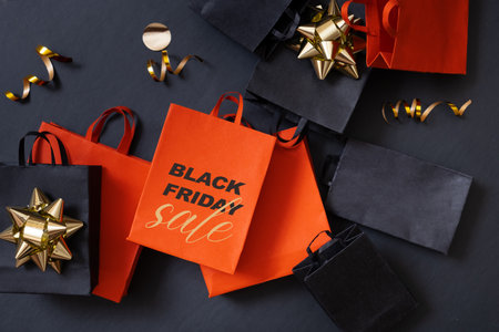 Black friday sale text, shopping concept. Red and black paper shopping bags with decorations on black backgroundの写真素材