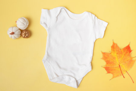 Baby clobodysuit mock-up top view with pumpkins and maple leaves on yellow background for your text or logo place in autumn seasonの写真素材