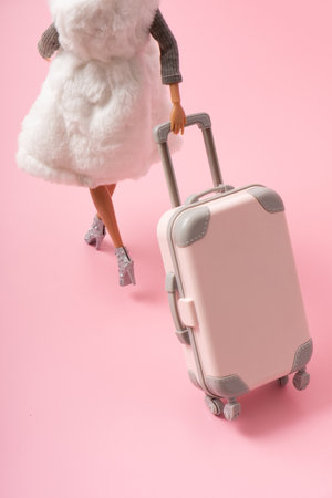 The doll carries a suitcase on wheels. Travel, vacation creative minimalistic concept.の写真素材