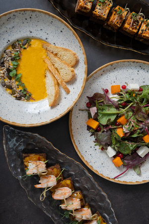 Pumpkin salad and soup, shrimp and marinated cheese canapes on dark background top view, flat lay.の写真素材