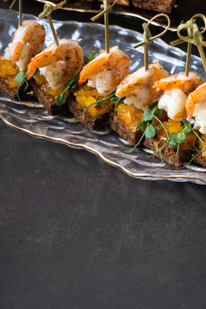 Shrimp and mango chutney canapes in glass plate on dark background with copy space. Mini sandwich, catering concept.の写真素材