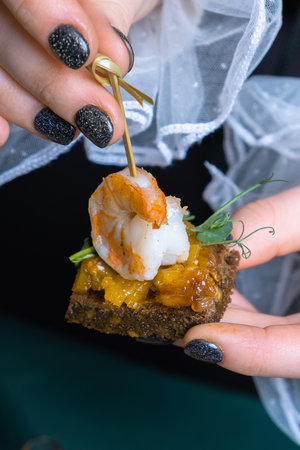 Shrimp and mango chutney canapes in female fingers. Mini sandwich on the party.の写真素材