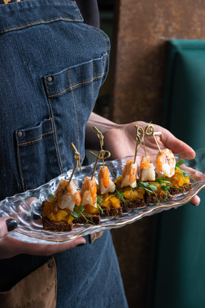 Canapes with shrimp chutney and mango on a plate in the hands of a waitress. Service area concept.の写真素材