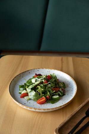 Fresh salad with arugula, cherry tomatoes, cucumbers in a plate against cafe interior.の写真素材