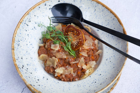 Bolognese in a bowl decorated dry tomato and microgreen on a wooden table top view, flat lay.の写真素材