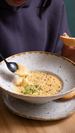 A spoon in the hands of a woman with a plate of cheese cream soup with nuts and greens.の写真素材