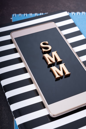 Abbreviation SMM made with wooden letters on phone, top view. Social Media Marketing.