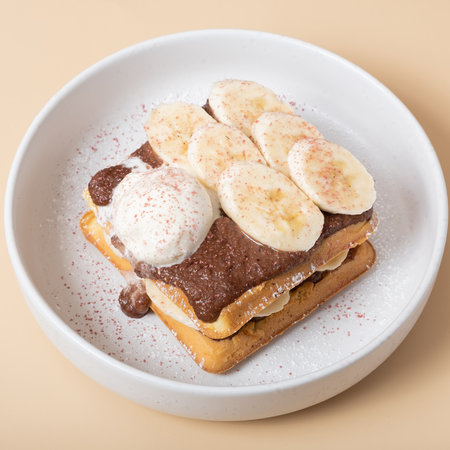 Belgian waffles with banana and chocolate sauce on a beige background.の写真素材