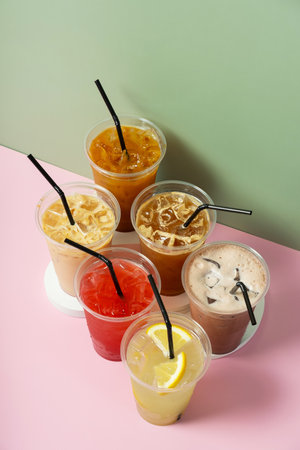 Takeaway glasses of summer drinks with ice. Lemonade and coctails on colored background.