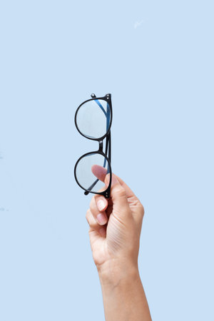 Eyes glasses in female hands on blue background with copy space. School supplies for back to school...