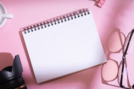 Blank notebook, SLR camera with glasses on desktop top view on pink background. Learning...