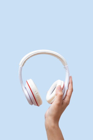 A female hand holds white headphones on a blue background