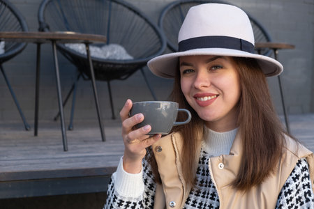 Beautiful brunette in a hat and autumn wardrobe with a cup of coffee outdoor.の写真素材