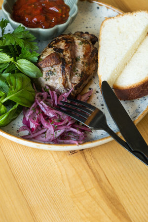 Fried pork meat with sauce, bread, pickled onion and greens on the plateの写真素材