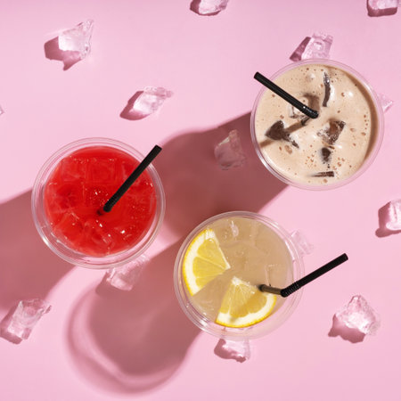 Three takeaway glasses of summer drinks with ice. Lemonade on colored background.