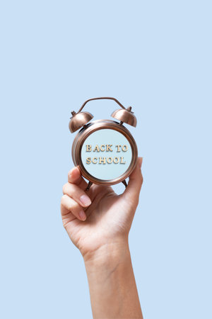 A woman's hand is holding an alarm clock with the inscription Back to school. High quality photoの写真素材