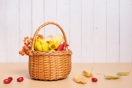 Autumn harvest basket with corn, apples, zucchini and peppers on a wooden background decorated with autumn flower and mountain ash.の写真素材