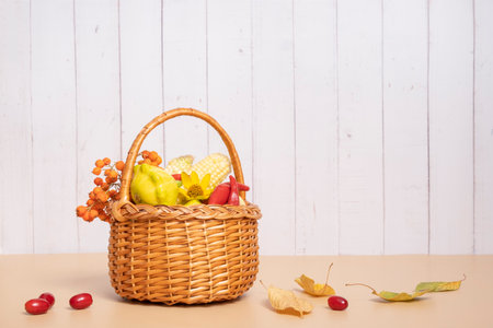 Autumn harvest basket with corn, apples, zucchini and peppers on a wooden background decorated with autumn flowerの写真素材