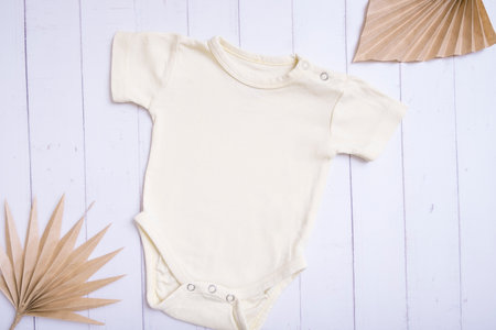 Yellow baby bodysuit mockup for logo, text or design on wooden background with palm leaves top view.の写真素材