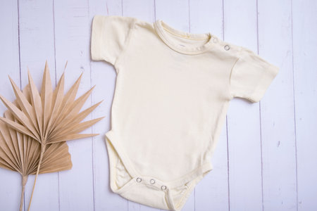 Yellow baby bodysuit mockup for logo, text or design on wooden background with palm leaves top view.の写真素材