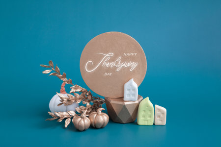 Still life of gold and white pumpkins, acorns and miniature houses on a turquoise background. Minimalistic autumn concept with text happy thanksgivingの写真素材