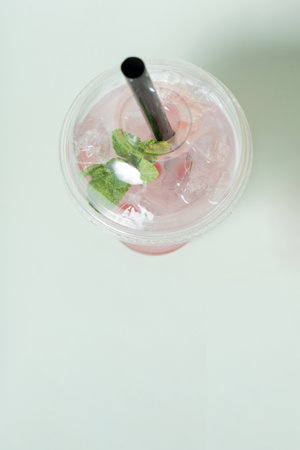 Cup of bubble tea filled with ice and fresh mint leaves rests on a light surface, showing its vibrant color and inviting appearance, perfect for a midday treat.の写真素材