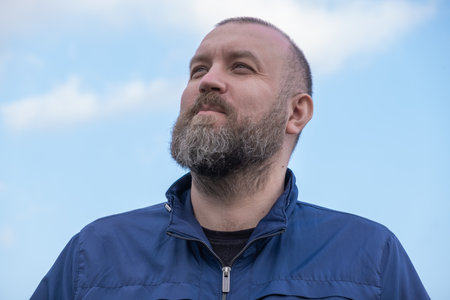 Man with beard looking up at a clear sky during a sunny day outdoors in a relaxed postureの写真素材