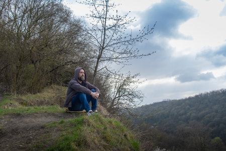 Man sitting quietly on a hillside contemplating nature during a cloudy day near a valleyの写真素材