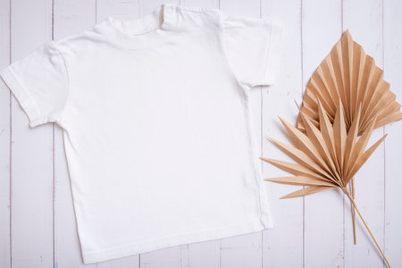 White children's t-shirt mockup for logo, text or design on wooden background with palm leaves top view.の写真素材