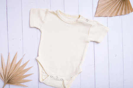Yellow baby bodysuit mockup for logo, text or design on wooden background with palm leaves top view.の写真素材