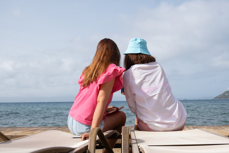 Friends enjoying a relaxed moment by the sea while sitting on lounge chairs at the beach.の写真素材