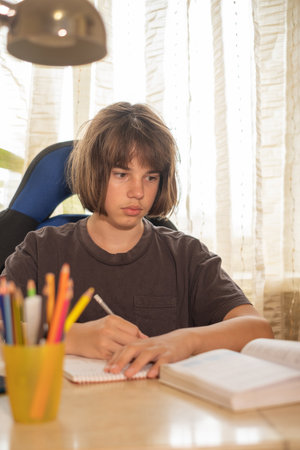 A young person sits at a round desk in a well-lit study, engrossed in reading a book