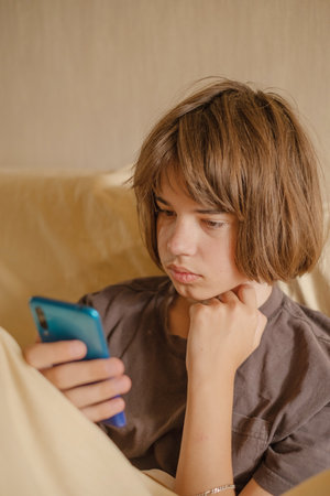 Teenage boy relaxing on sofa while using smartphone in cozy living room during afternoon time.の写真素材