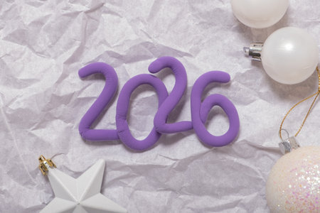 Bright purple numbers represent the year 2026 surrounded by decorative ornaments on crinkled paper,...