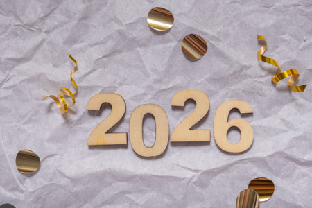 Festive golden decorations and confetti surround the wooden numbers for the year 2026 against a...