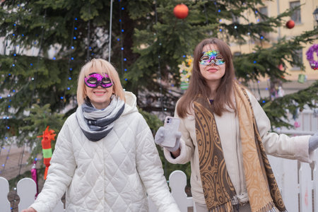 Friends enjoying a festive celebration with colorful masks during winter festivities in a city squareの写真素材