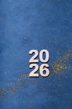 Wooden numbers display 2026 on a blue background with golden sparkles for a festive atmosphere