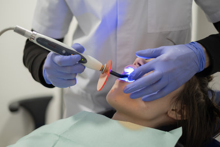A patient lies on a dental chair while a dental professional performs a procedure. The room is...