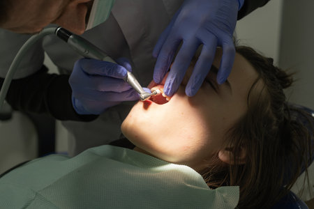 A young woman lies back in a dental chair while a dentist examines her teeth using specialized tools. The clinic has bright lighting and a calm atmosphere, creating a professional setting.の写真素材
