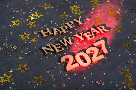 Happy New Year 2021 is written in bright letters. Small stars and shiny decorations are spread on the table. It is a festive setting for celebration.