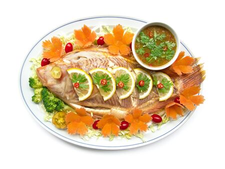 Steamed fish (Tilapia fish) in lemon sauce with Thai spicy sauce or seafood sauce in dipping bowl decorate with carved carrots tomato vegetables style healthy food, diet food top viewの写真素材