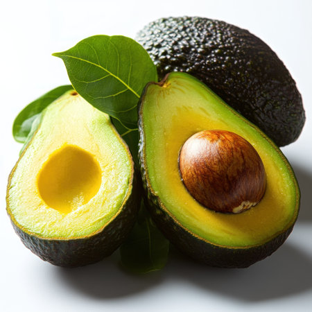 Freshly cut avocados reveal their creamy interior beside lush green leaves.の素材