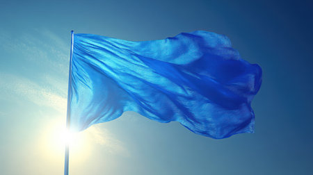 The blue flag flutters gracefully in the warm sunlight against a clear sky backdrop.の素材