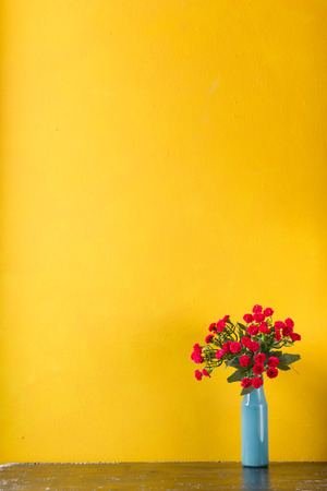 Red flowers in vase on yellow background.の写真素材