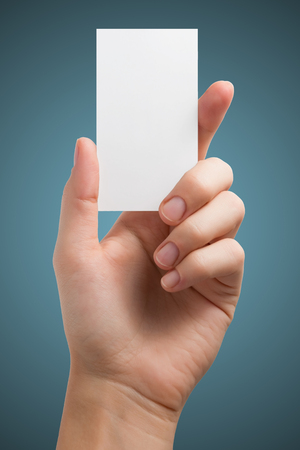 Hand holding white blank business visit card, gift, ticket, pass, present isolated on blue background. Copy space for text. Corporate identity package business card Template for ID.の写真素材