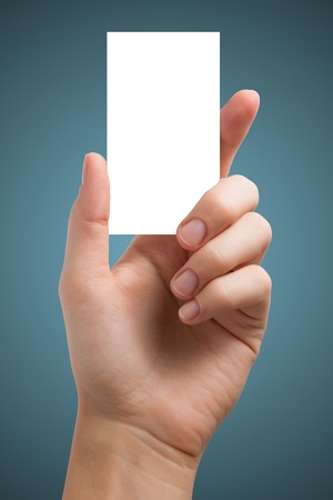 Hand holding white blank business visit card, gift, ticket, pass, present isolated on blue background. Copy space for text. Corporate identity package business card Template for ID.の写真素材